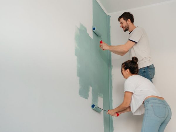A young couple collaborates on painting a wall with rollers, highlighting teamwork and home improvement.